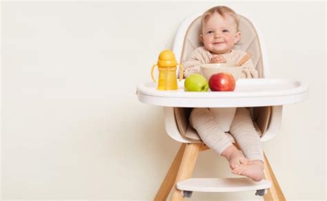 kūdikis sėdi maitinimo kėdutėje ir valgo gabaliukais